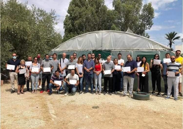 Participants d'une formation posant avec leur attestation devant une serre